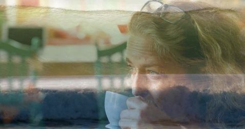 Mature woman holding cup gazing through coastal double exposure conveying contemplation