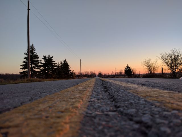Vibrant image of a road leading into the distance during sunset, with clear sky and trees in the background. Ideal for illustrating themes of travel, adventure, journey, solitude, and peaceful evening. Suitable for blogs, social media posts, advertisement campaigns, travel brochures, and inspirational content.