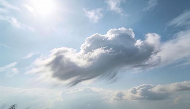 Billowing cumulus cloud rising above horizon, rim-lit by sun with wispy cirrus accents