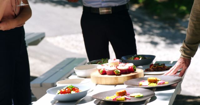 Friends enjoying gourmet food served in plates during a casual outdoor picnic. Ideal for use in promotional material for summer gatherings, lifestyle blogs, social events, and dining experiences.