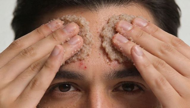 Man exfoliating forehead with grainy circular scrub pads closeup skincare texture
