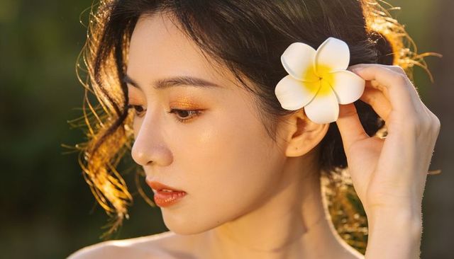 Holding plumeria at ear during golden hour beauty portrait with glowing skin and rim light