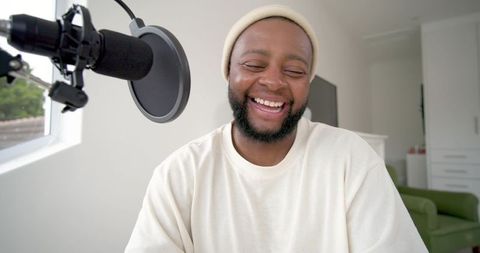 Laughing podcaster recording in bright minimal home studio with microphone and pop filter