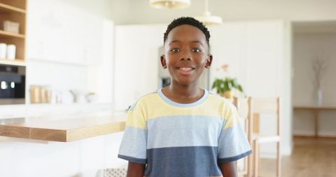 African american boy standing and smiling in bright modern kitchen wearing striped tee