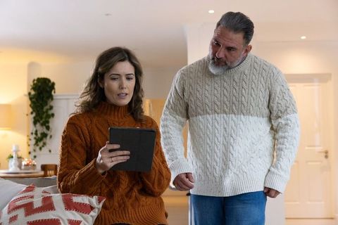 Mature couple sharing tablet on sofa wearing cozy knit sweaters in living room