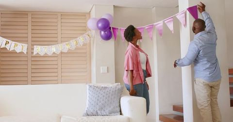 African American Couple Decorating Living Room with Pink and Purple Bunting and Balloons