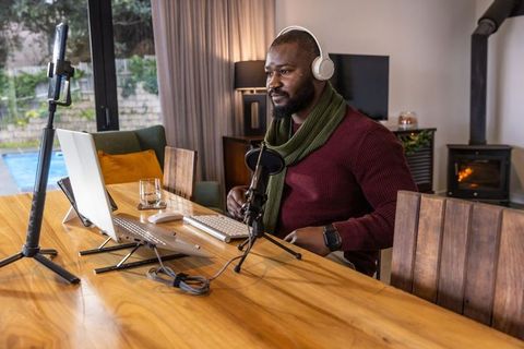 African american man recording podcast home studio with laptop microphone and headphones