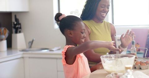 African mother and daughter baking together at modern kitchen counter, stirring batter