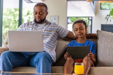 African american father and son working and relaxing on sofa with laptop and tablet