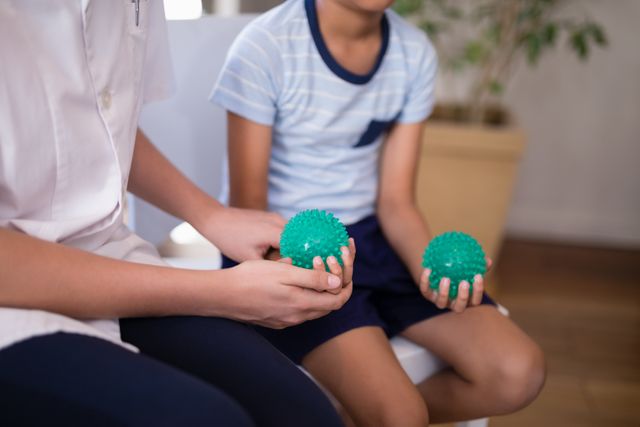 Midsection of female therapist and boy holding stress balls at hospital ward