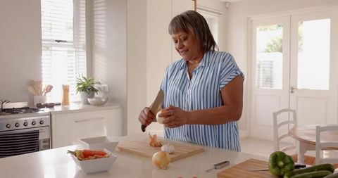 Senior Woman Peeling Onion Preparing Meal in Modern Kitchen