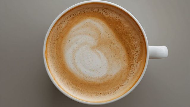 Overhead latte with creamy milk foam swirl in white ceramic cup on gray minimal tabletop
