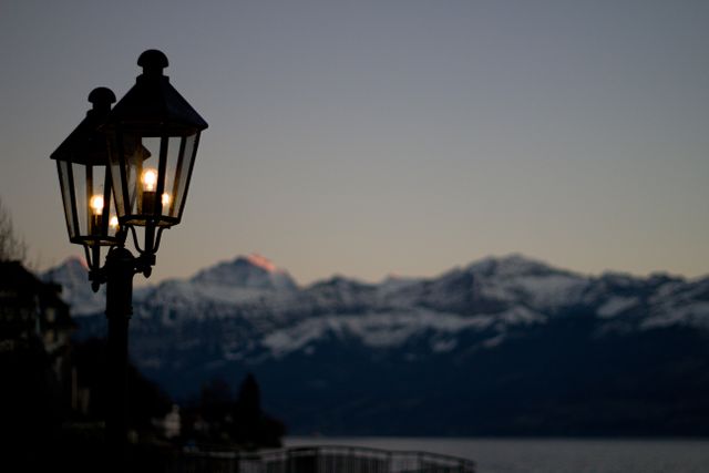 Vintage street lamp glowing during twilight near snow-capped mountains - Download Free Stock Photos Pikwizard.com