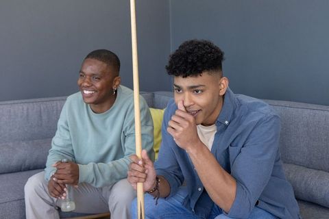 Multiracial friends laughing and playing pool on modern living room couch
