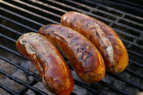 Grilling bratwurst sausages on charred grill bars for backyard barbecue and summer cookout