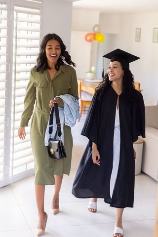 Graduate celebrating at home with supportive friend in cap and gown