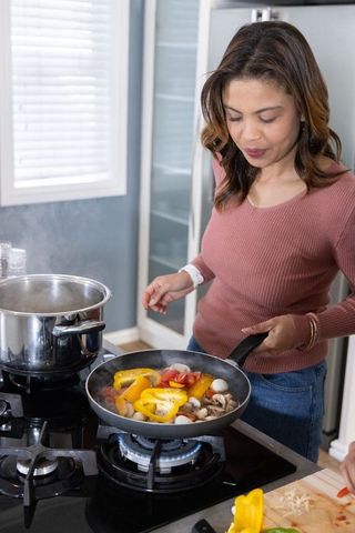 Woman cooking colorful bell peppers and mushrooms on gas stove in bright home kitchen