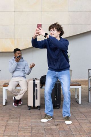 Two friends taking selfie at urban transit plaza with suitcases and backpacks