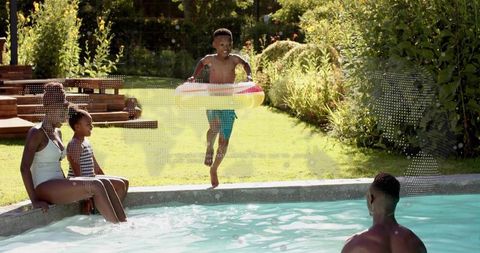 Black family enjoying backyard pool day with boy running and jumping with inflatable ring