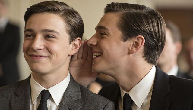 Whispering teenage boys wearing formal suits during ceremony, smiling and sharing secret