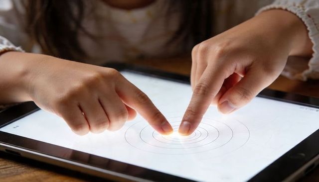 Child hands tapping tablet screen with concentric touch rings, closeup technology learning