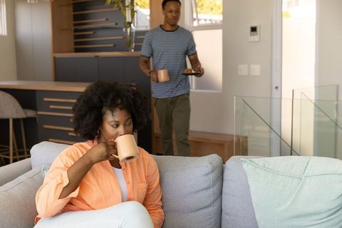 African American Couple Relaxing on Sofa Sipping Coffee in Bright Open-Plan Living Room