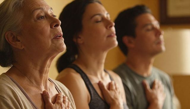 Multigenerational trio practicing mindful breathwork with hands over heart in calm moment