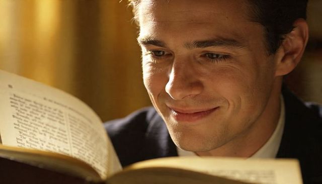 Young professional reading vintage book in warm golden light, smiling with quiet focus