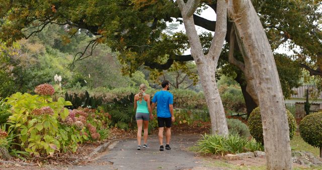 Couple walking together along a tree-lined path in a park. Captures essence of outdoor exercise, peacefulness, and nature. Ideal for promoting fitness, wellness, recreation, and harmonious lifestyle.