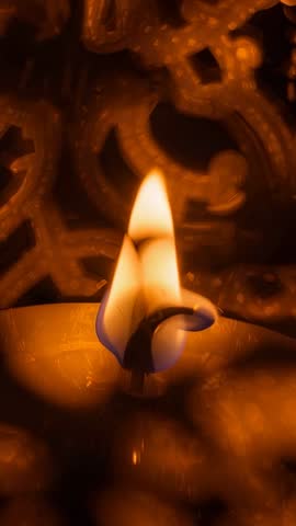Vertical video showing candle flame flickering at temple altar illuminating ornate lattice