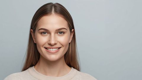 Smiling young woman wearing beige sweater neutral studio headshot natural beauty