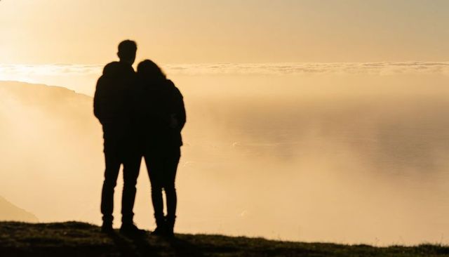 Silhouetted couple embracing on cliff at golden hour overlooking misty sea