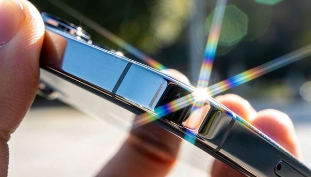 Sunlit smartphone edge with chrome reflection and rainbow starburst glare macro close-up