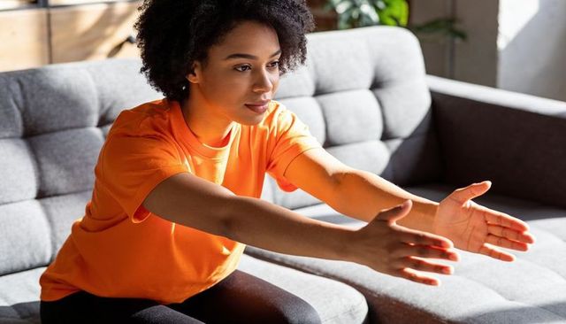 Young woman stretching on sofa in orange t-shirt for home wellness and mobility routine