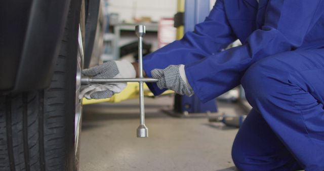 Mechanic in blue uniform changing car tire in garage - Download Free Stock Images Pikwizard.com