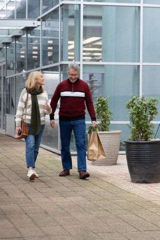 Senior couple walking and chatting outside modern glass building holding shopping bag