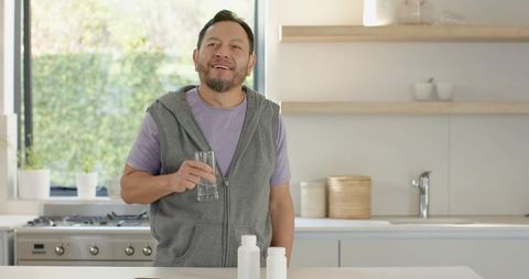 Mature Asian Man Drinking Water with Supplement in Natural Light Kitchen