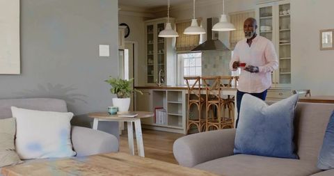 Senior man holding red teacup and saucer in open-plan kitchen livingroom with rustic decor