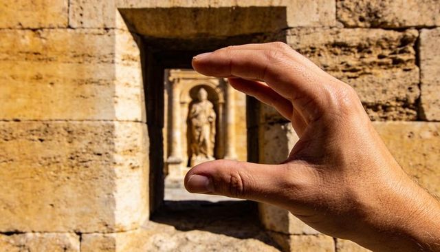 Right hand framing carved statue through sandstone opening, sunlit historic architecture