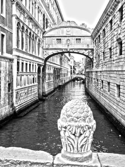 Depicts historic stone bridge over canal in Venice in monochrome, emphasizing architectural details. Suitable for travel brochures, historical articles, cultural exploration blogs, and European tour promotions.