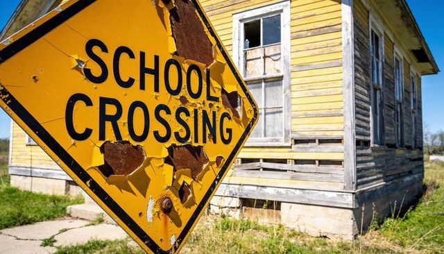 Peeling school crossing sign with rust and bullet damage leaning by abandoned schoolhouse