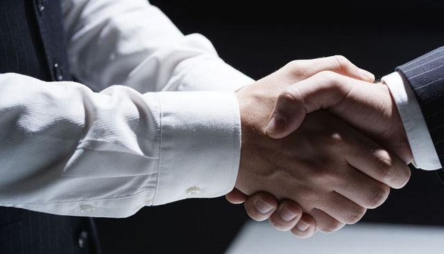 Business partners shaking hands in firm agreement close-up with suit cuffs pinstripe