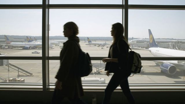 Silhouetted women walking through airport concourse past parked jets on tarmac