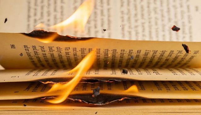 Burning book pages with glowing flames and flying embers close-up dramatic charred edges