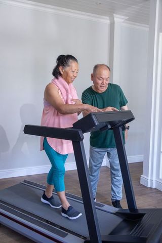 Chinese senior couple exercising at home with partner assisting on treadmill for wellness