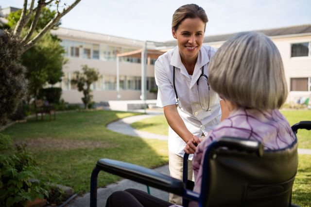 Doctor engaging with senior woman in wheelchair in outdoor setting. Ideal for use in healthcare, elderly care, medical services, nursing homes, and retirement community promotions. Highlights compassion and support in geriatric care.