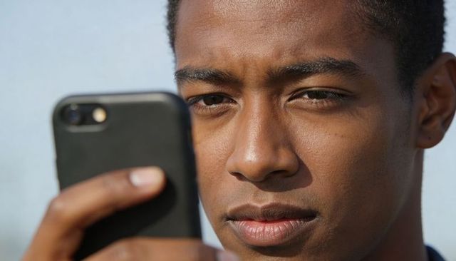 Young man holding smartphone, focusing on screen closeup outdoors, mobile technology portrait