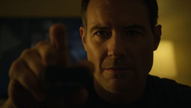 Moody cinematic closeup of man pointing remote at camera in dim living room evening