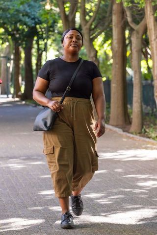African woman walking on tree-lined path wearing olive cargo pants and black crossbody bag
