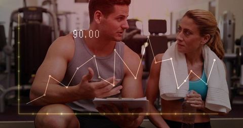 Fitness trainer coaching client in gym reviewing performance data and workout metrics